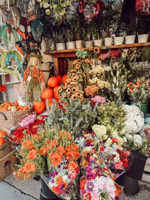 A vibrant floral display outside North Woolwich florist, showcasing an assortment of fresh flowers including orange and pink roses, white hydrangeas, purple and pink asters, and green foliage arranged