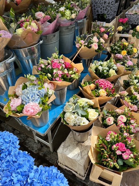 A vibrant display of freshly arranged flower bouquets and potted plants at North Woolwich florist, featuring pastel pink and white roses, blue hydrangeas, and various green foliage, all wrapped in bro