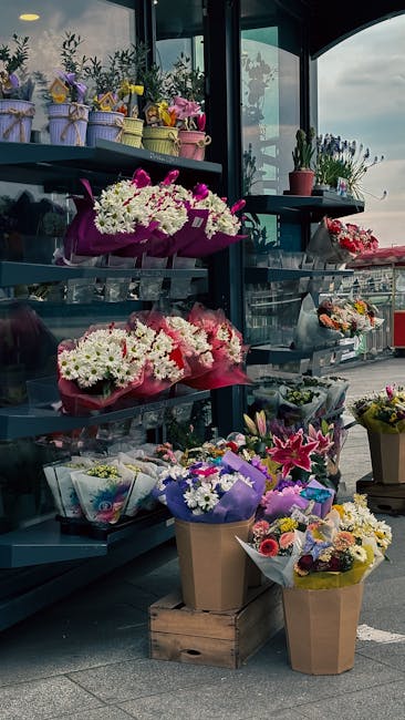 A display of various floral arrangements outside northwoolwichflorist.co.uk, featuring colorful bouquets with white, pink, purple, and yellow flowers. The arrangements include chrysanthemums, lilies,